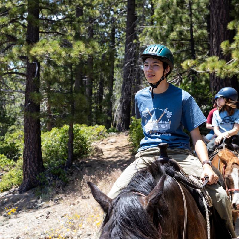 Scout on horseback on a forest trail at Camp Hi-Sierra, with more riders behind